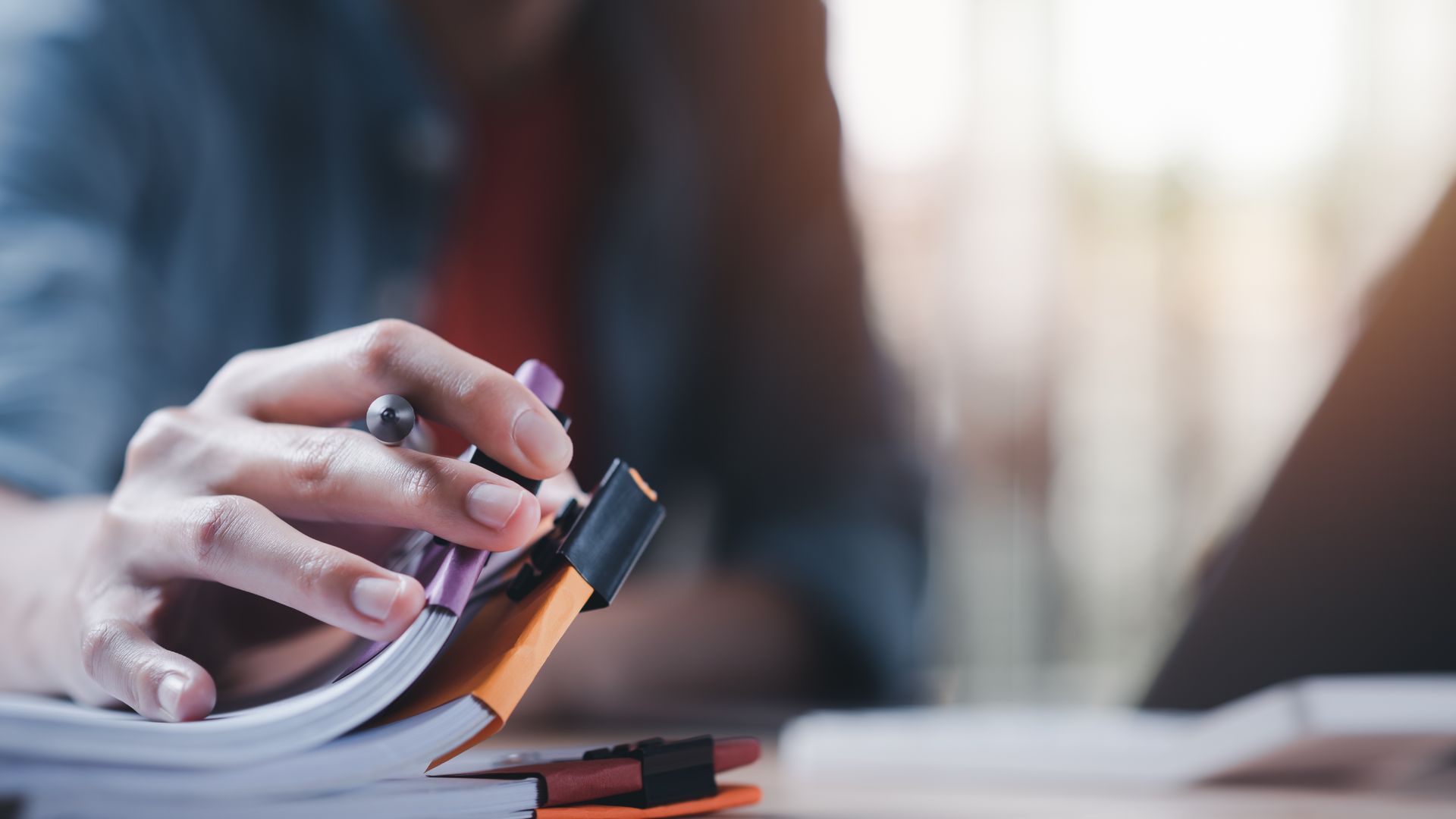 A person is holding a pen over a stack of books.