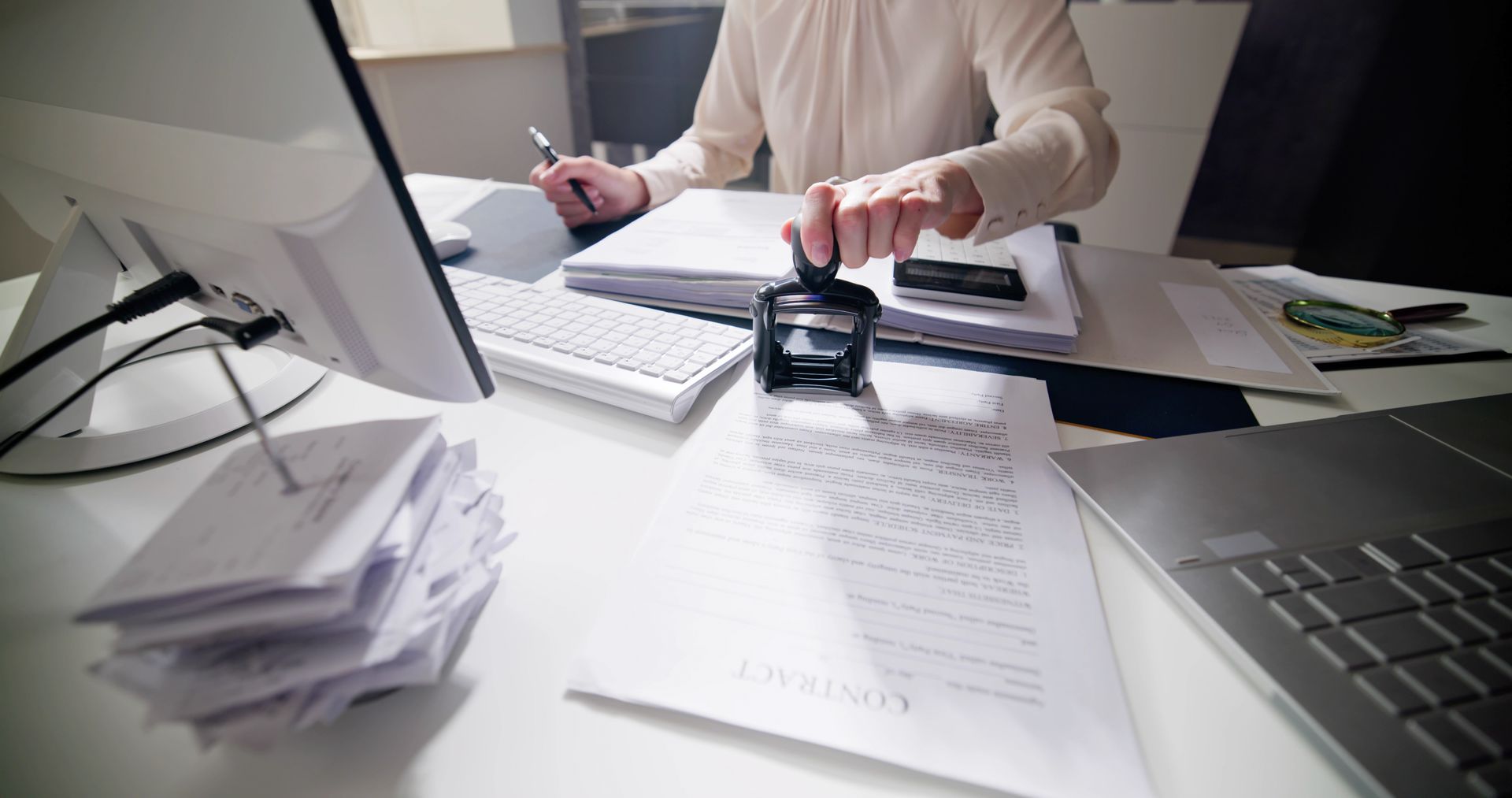 A woman is sitting at a desk using a stamp on a piece of paper.