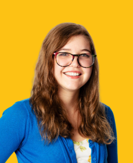 A woman with long hair is smiling in front of a yellow background.