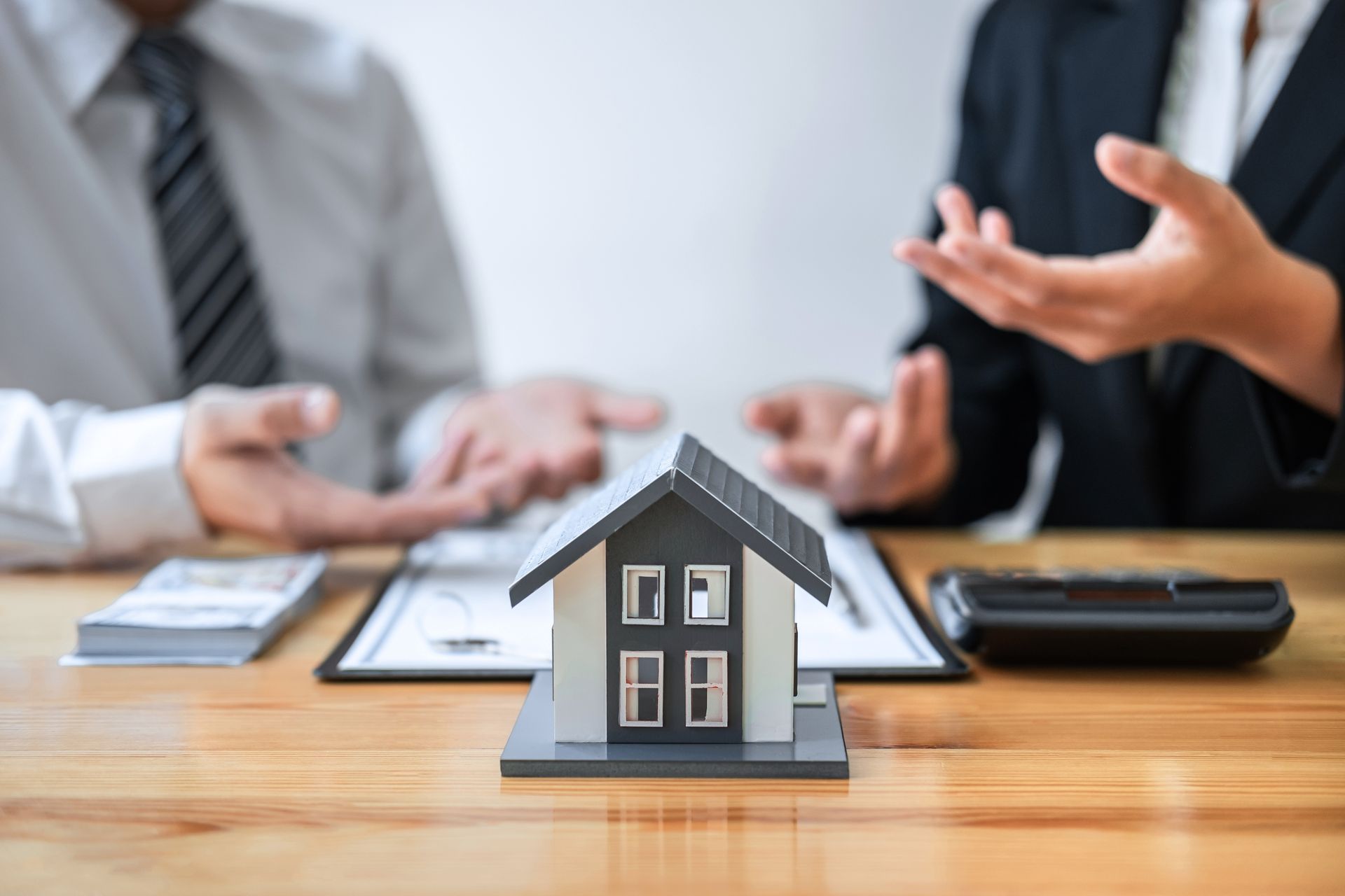 A man and a woman are sitting at a table with a model house on it.