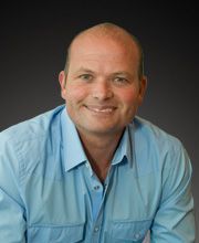 Professional headshot of Rob Popham wearing a light blue shirt, smiling against a dark gradient background.