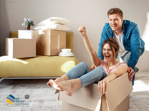 A man and a woman are sitting in a cardboard box in a living room.