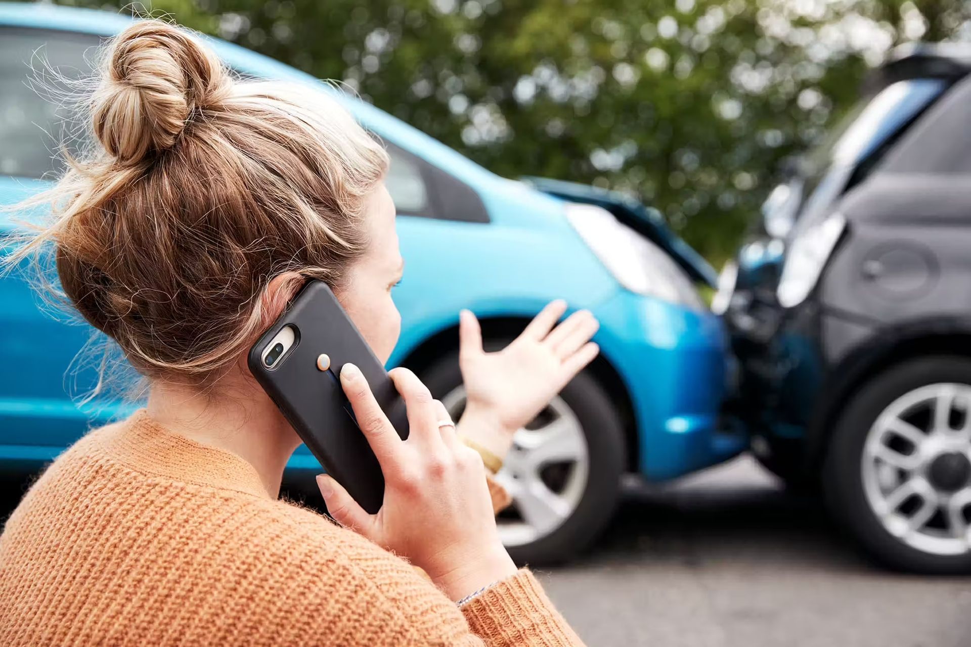 A woman is talking on a cell phone in front of a car accident.