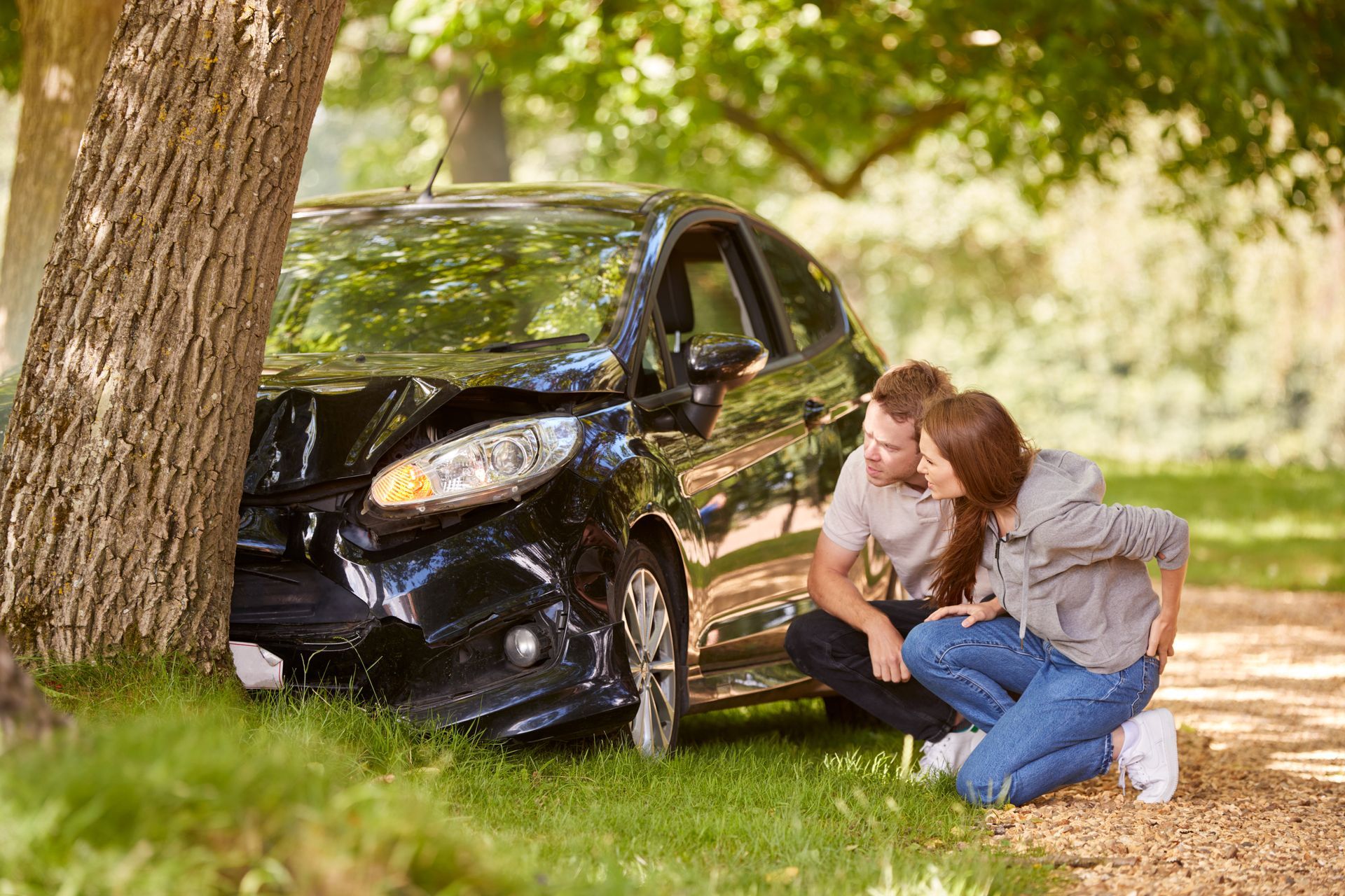 A man and a woman are sitting next to a damaged car.