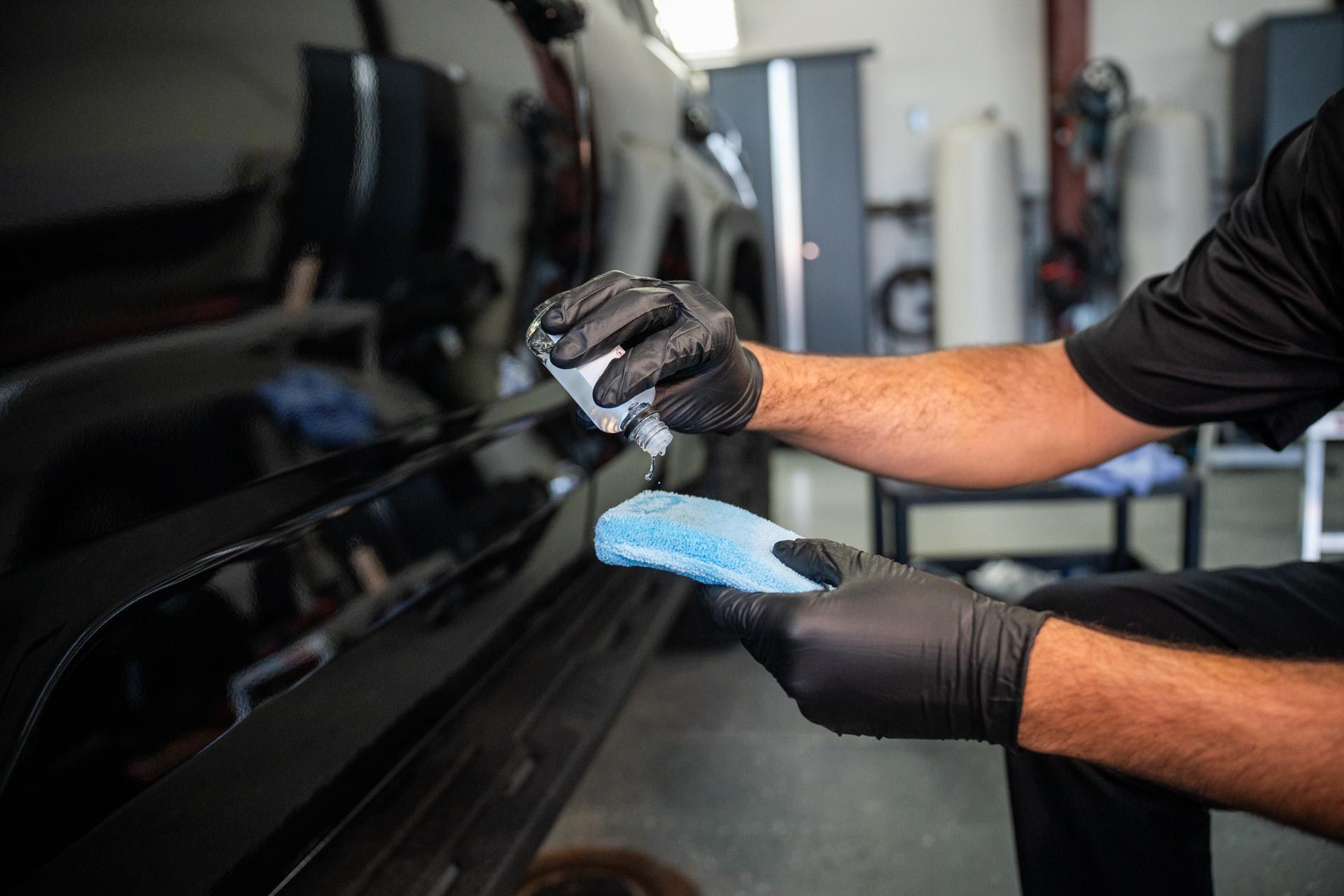 A man wearing black gloves is cleaning a car with a sponge.