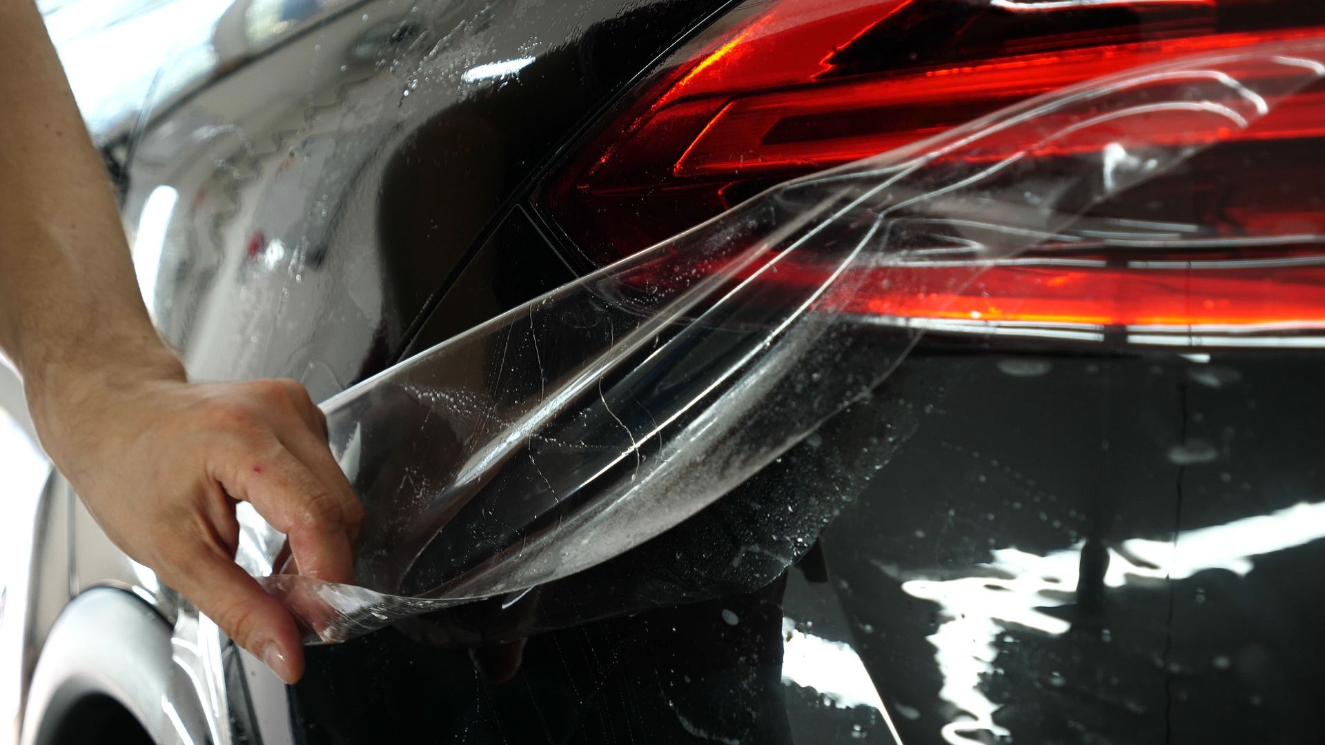 A person is applying a clear film to the back of a car.
