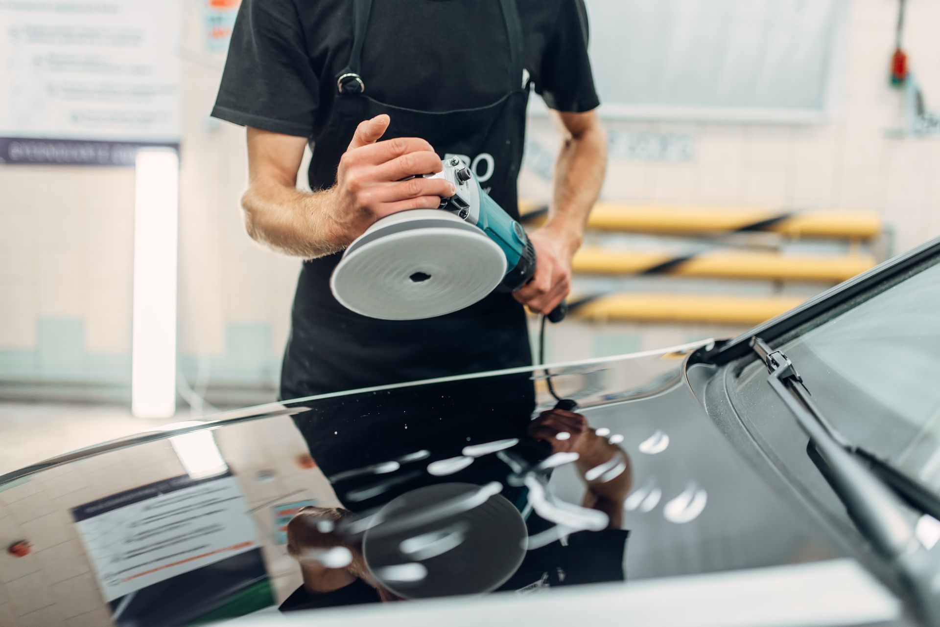 A man is polishing the hood of a car with a machine.