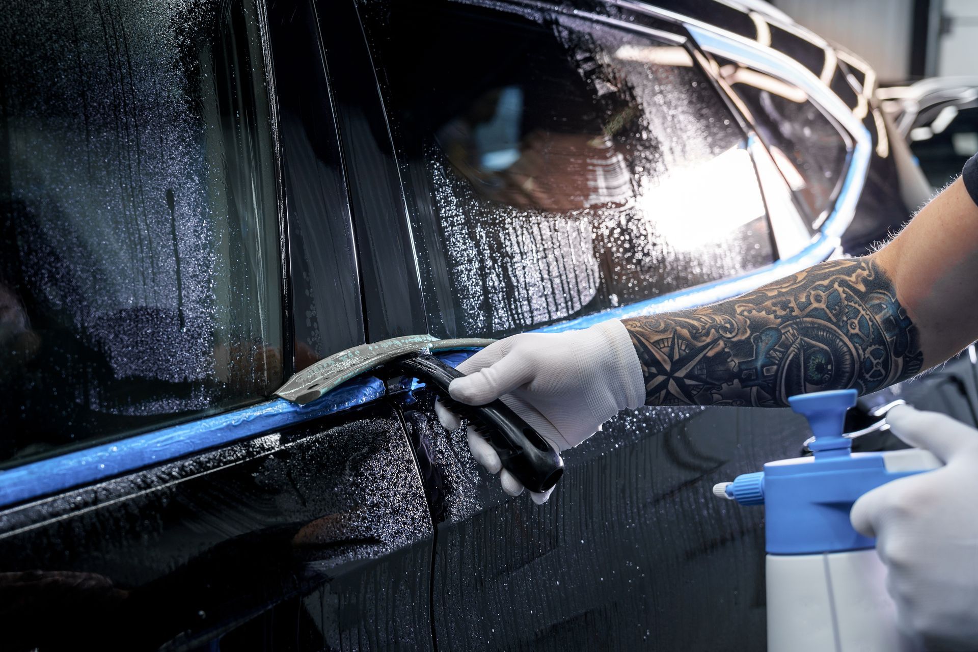 A person is cleaning a car with a spray bottle and a sponge.