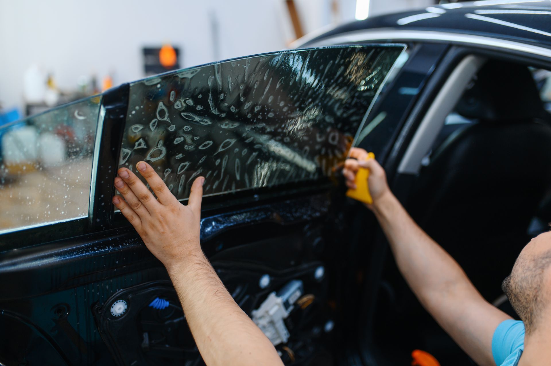 A person is applying tinted window film to a car window.