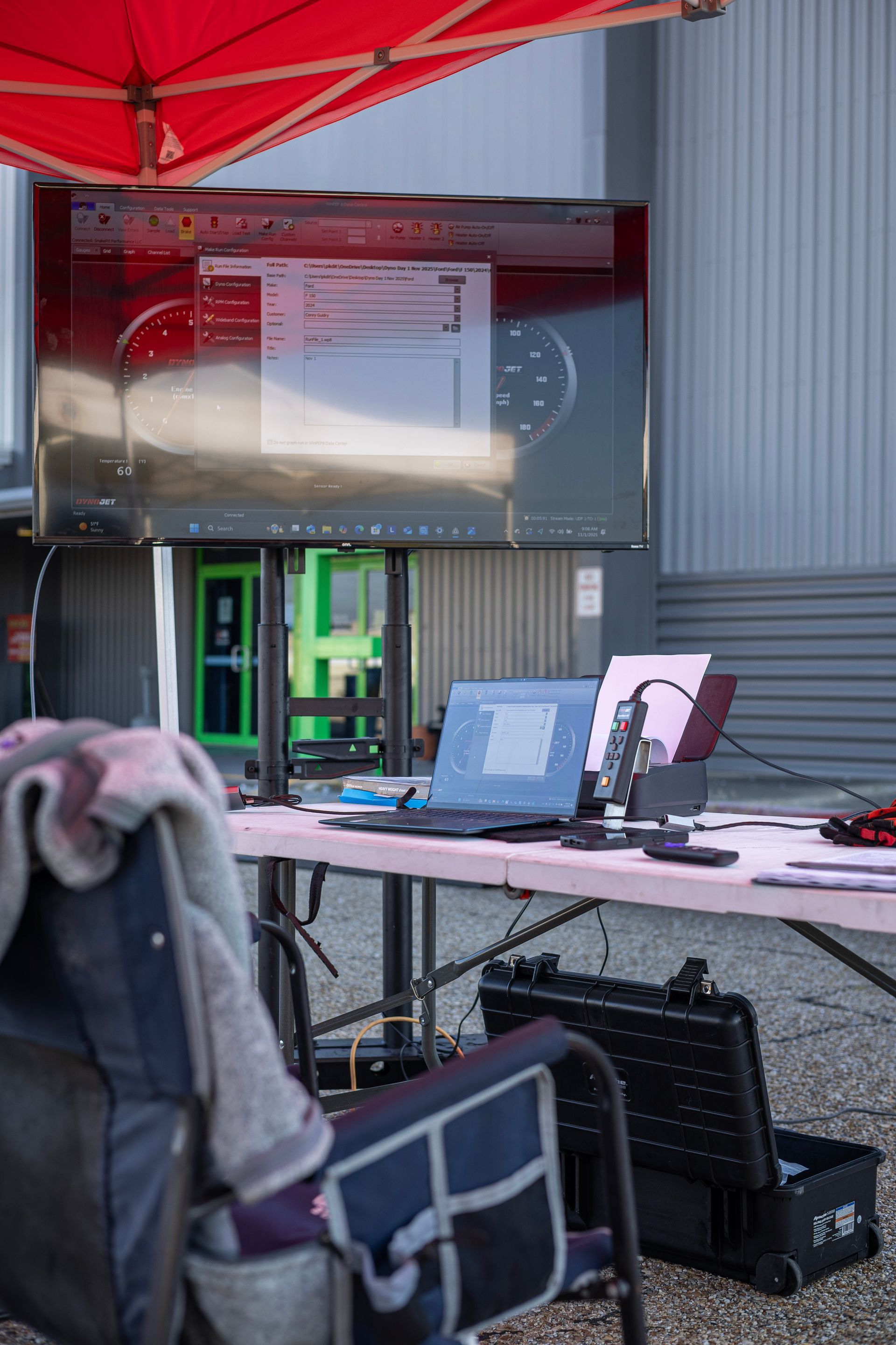 A workstation with a laptop, monitor, and equipment outside under a red umbrella.