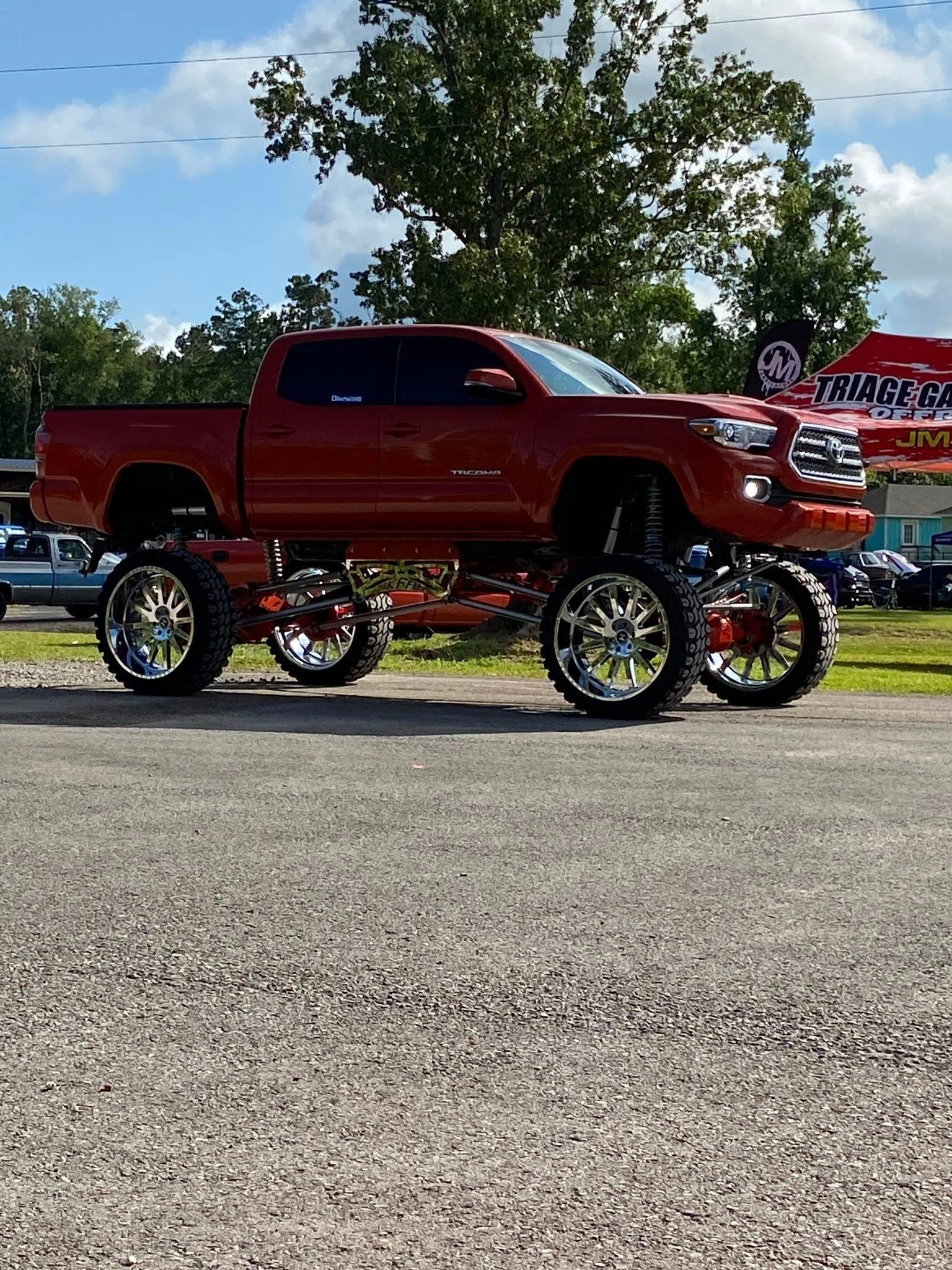 Red lifted Toyota pickup truck with chrome wheels on a gravel lot under a blue sky.