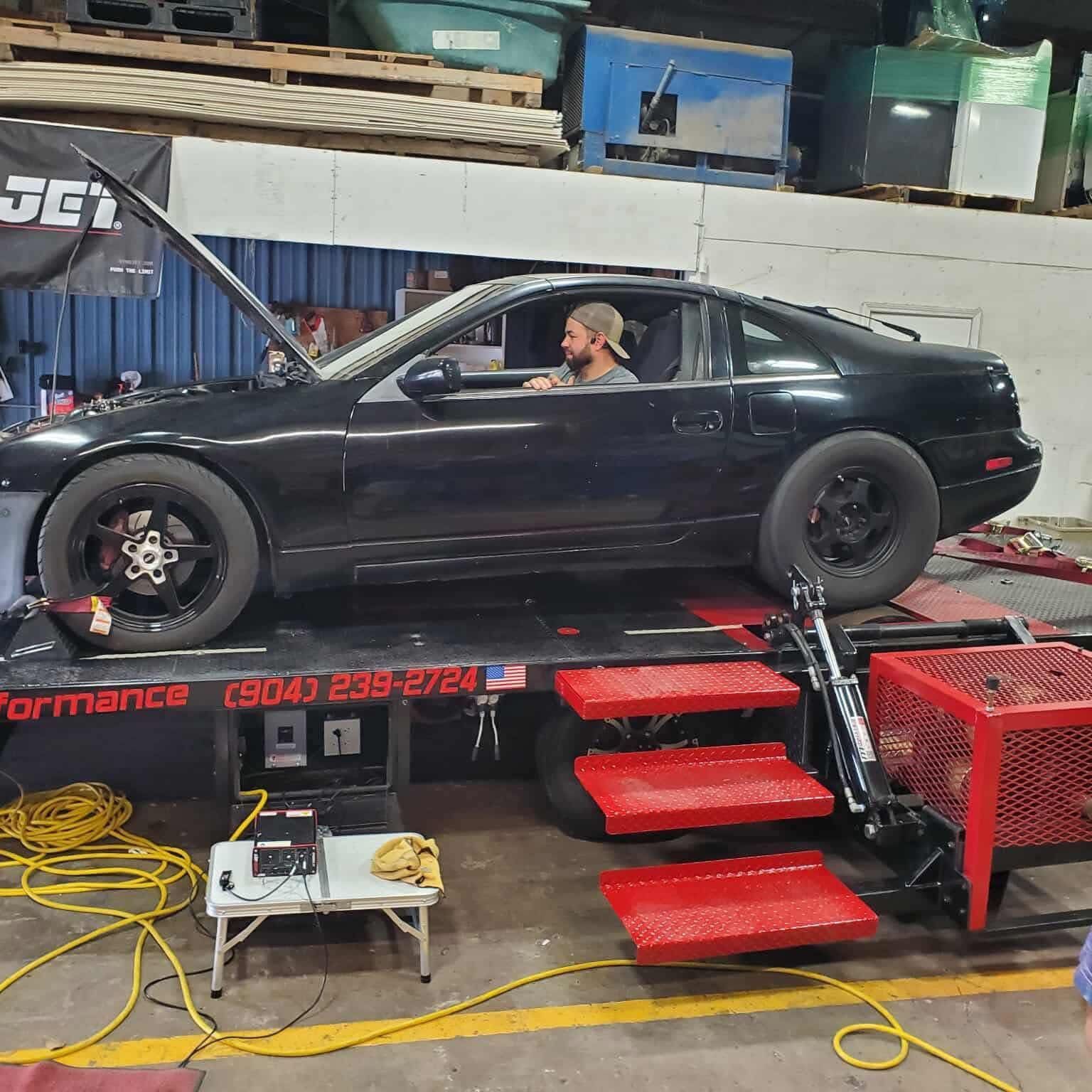 Black car on a dyno; a man in the driver's seat. Inside a garage.