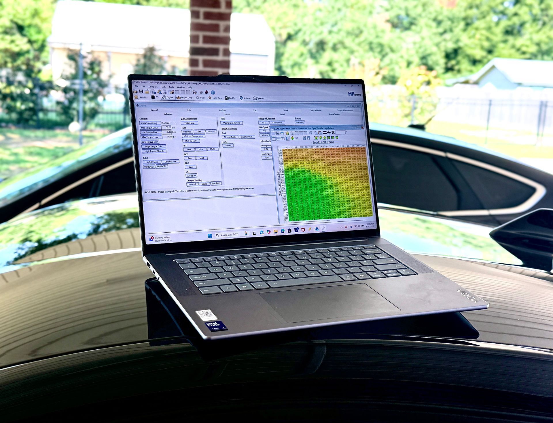 Laptop displaying software on a car roof, likely for vehicle diagnostics/tuning. Green, yellow, and red color data visible.
