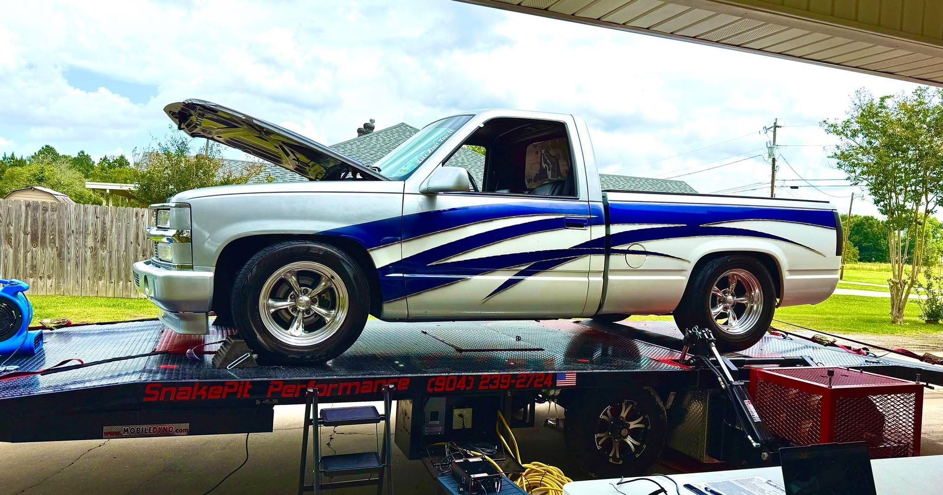 White and blue pickup truck on a tow truck with its hood open, outdoors.