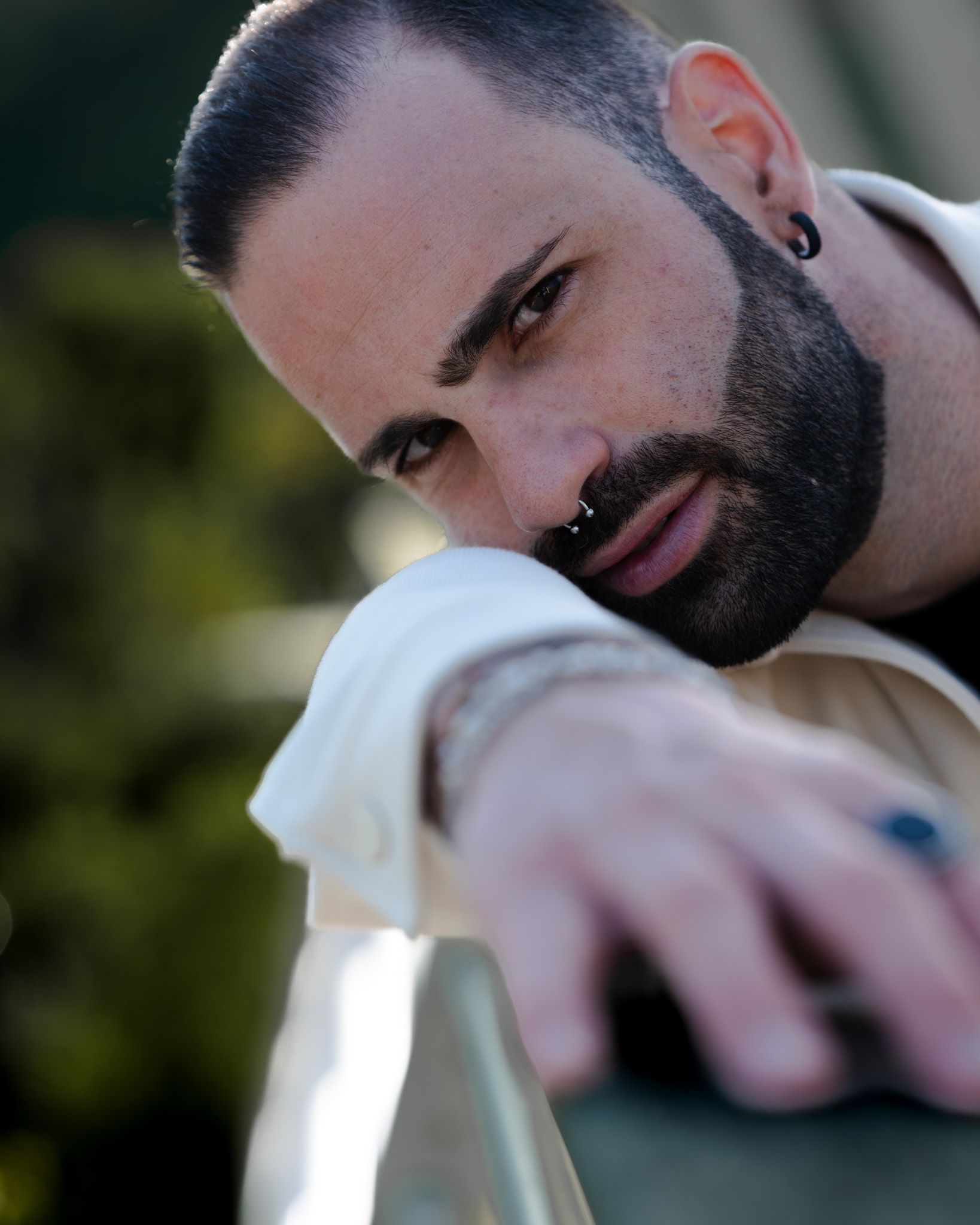 Uomo con barba scura e anello al naso, proteso in avanti con un'espressione seria.