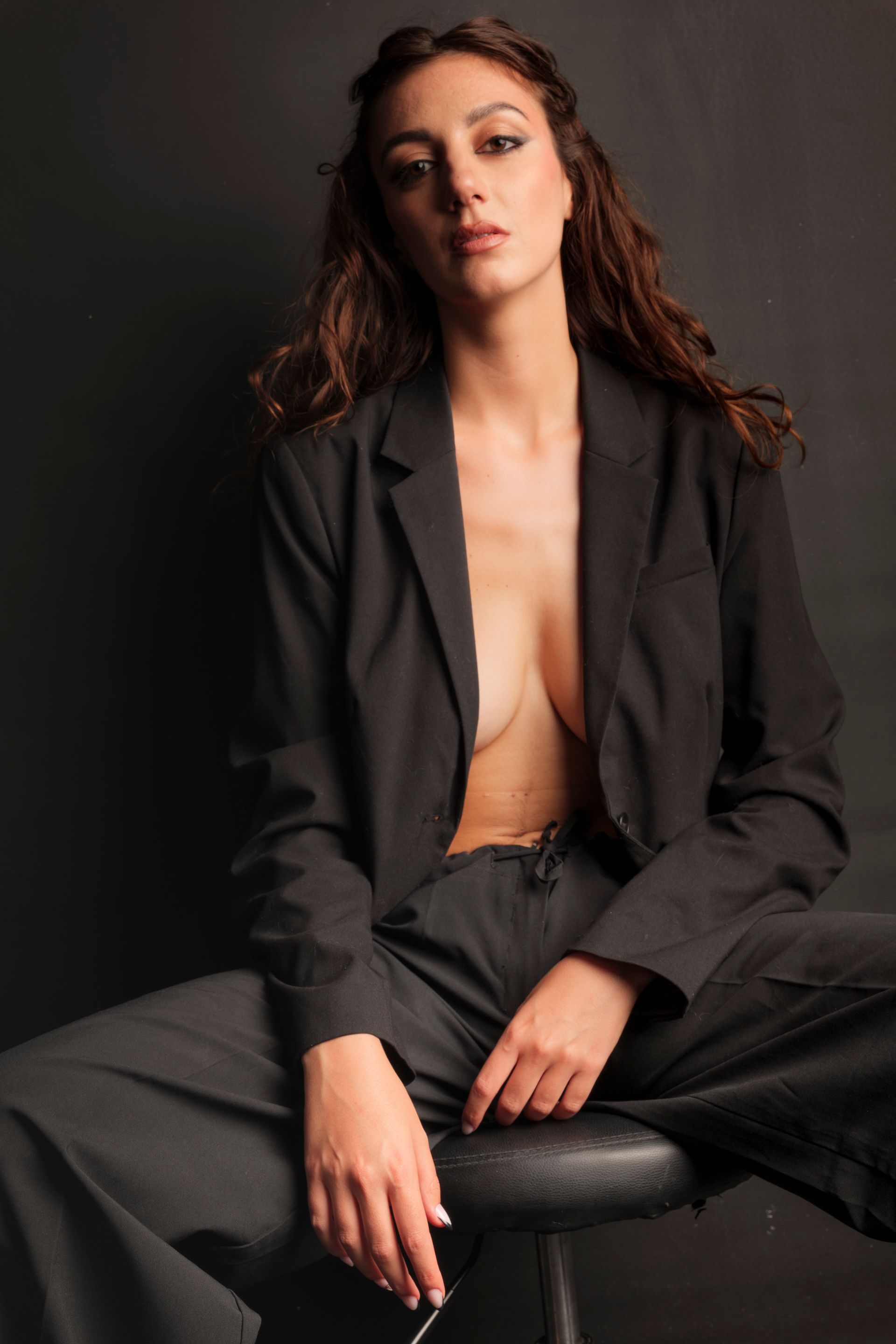 Donna in abito nero, giacca sbottonata, seduta su uno sfondo scuro.