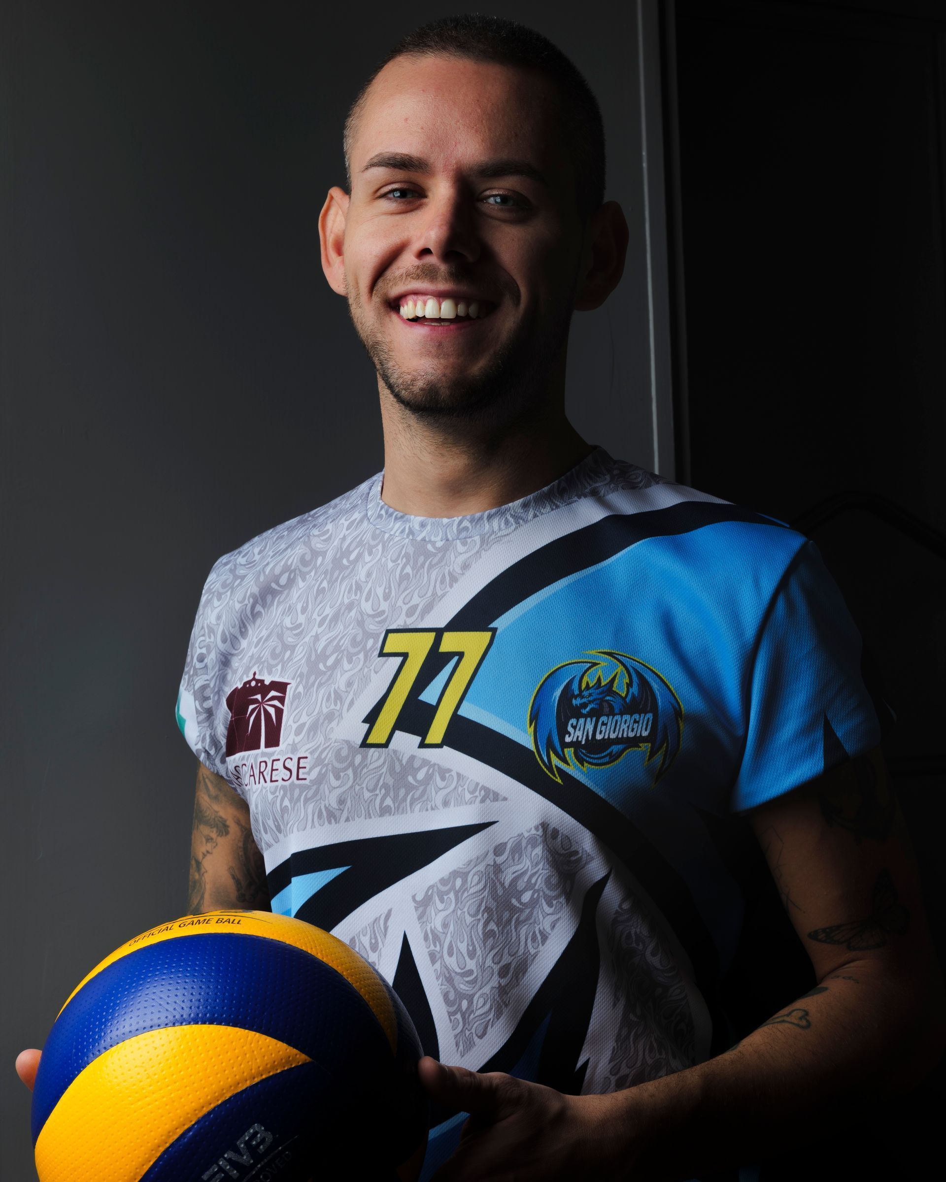 Un uomo con la maglia da pallavolo sorride tenendo in mano la palla.