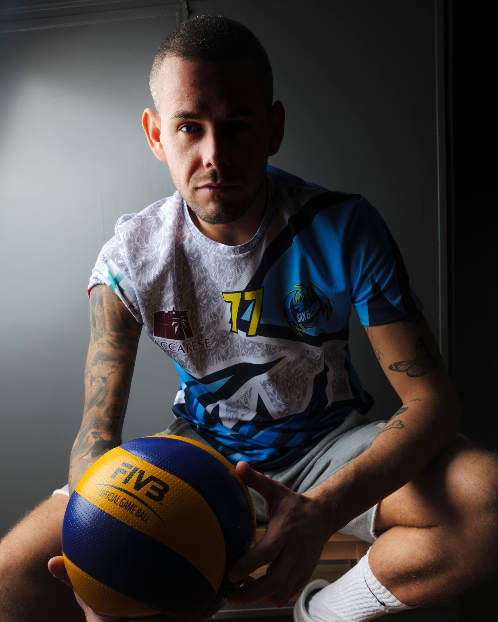 Uomo con tatuaggi che tiene in mano un pallone da pallavolo e indossa una maglia.