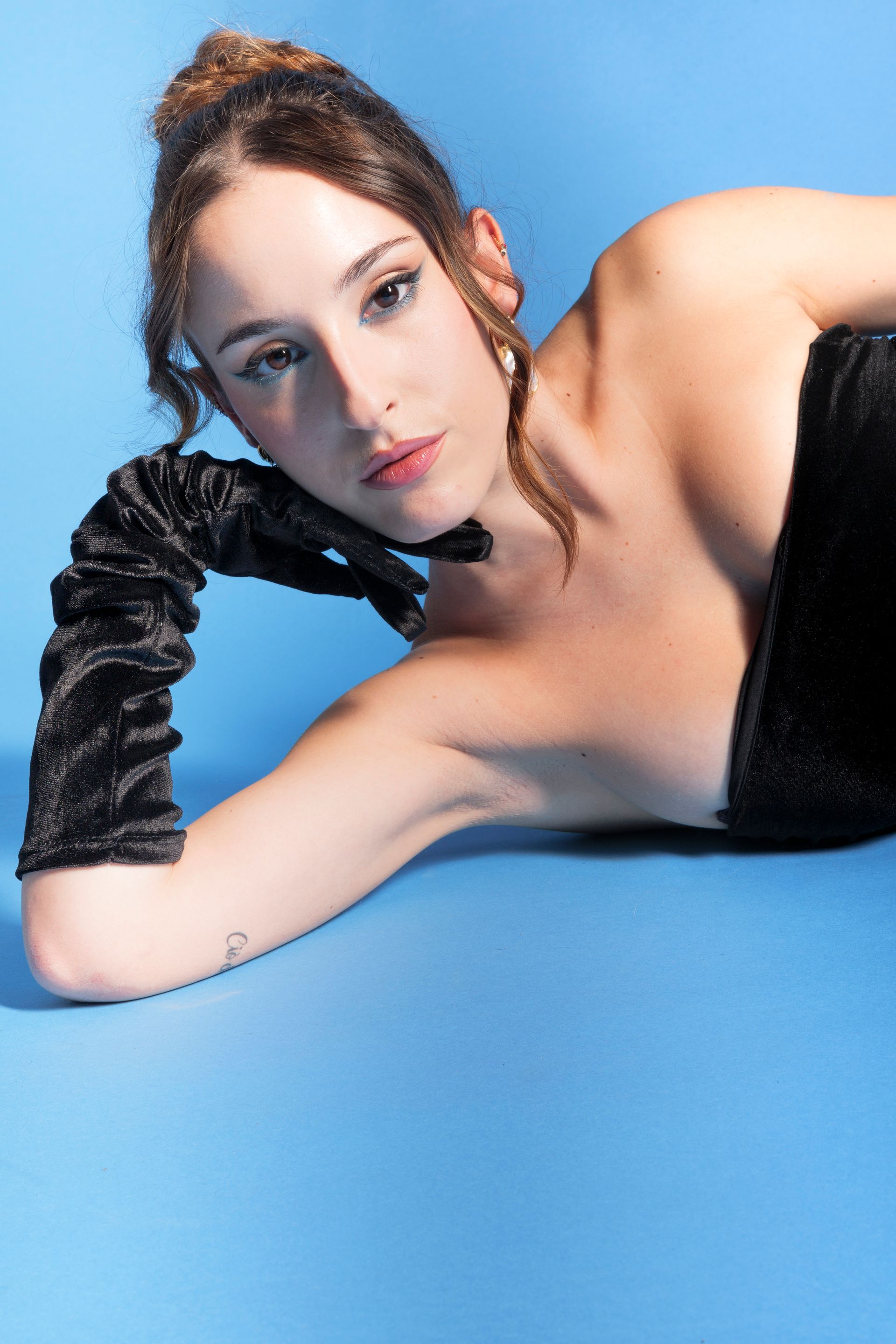 Donna in abito nero e guanti, in posa su sfondo blu.