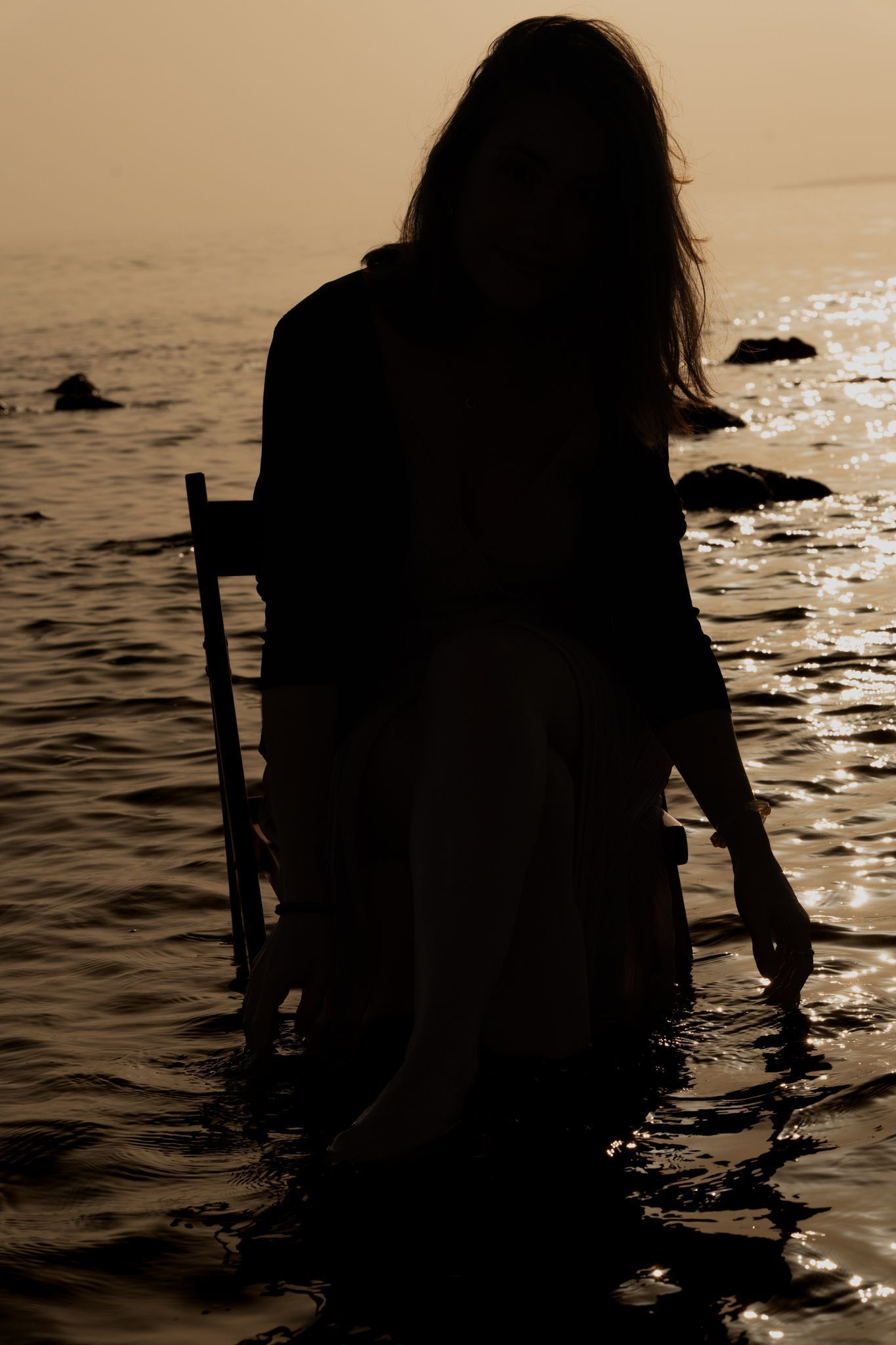 Sagoma di una persona in acqua, che tiene in mano un bastone, con la luce dorata del sole che si riflette sull'acqua.