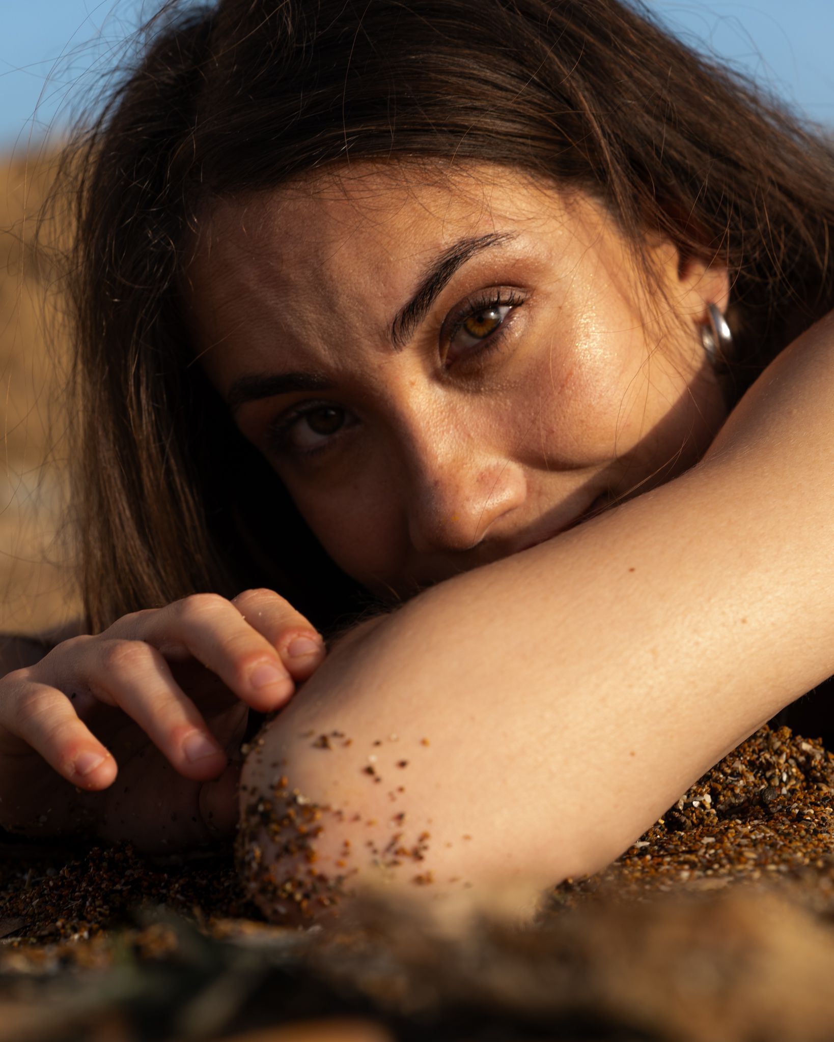 Donna sulla spiaggia che guarda la telecamera, capelli castani, braccio sulla sabbia.