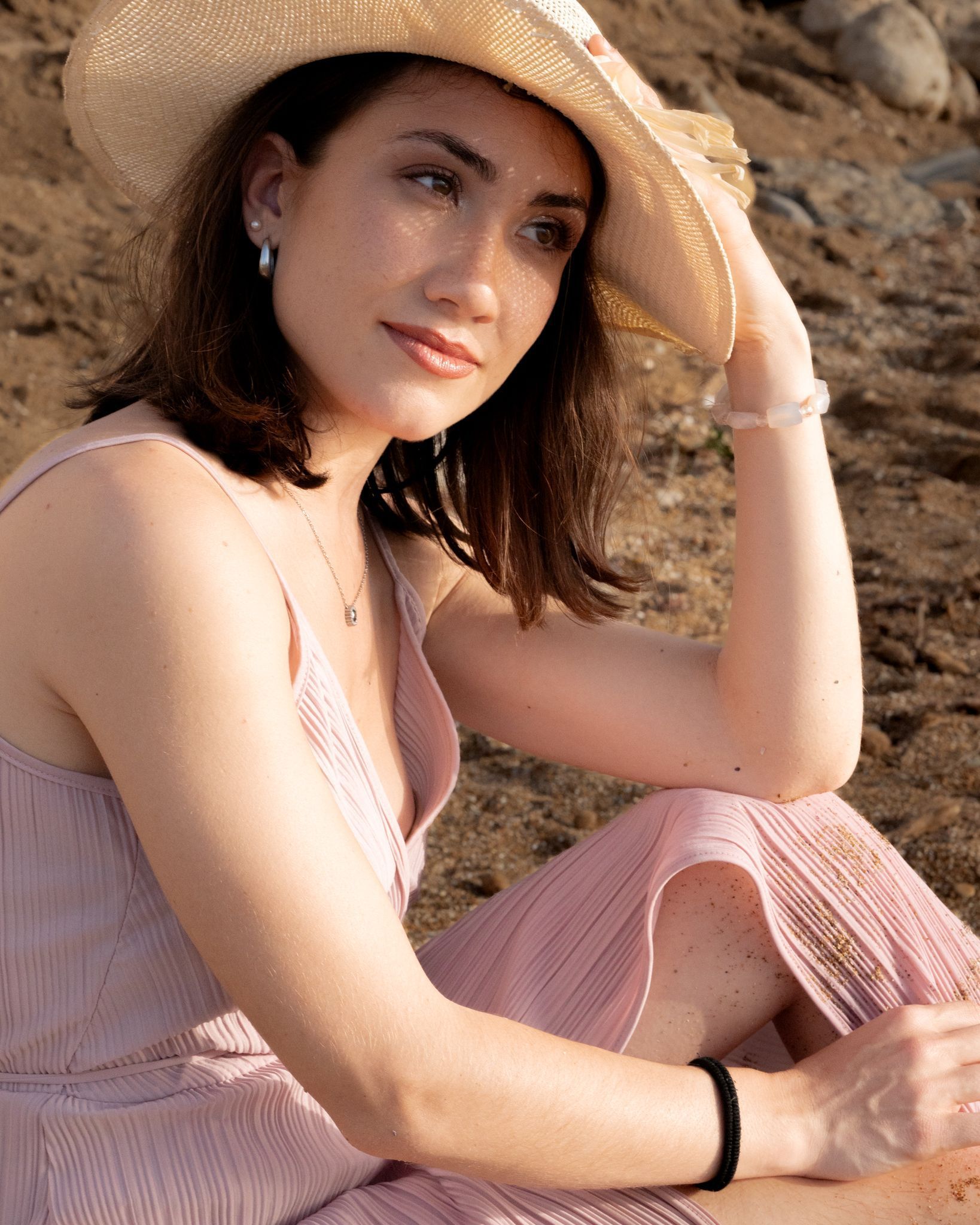 Donna con abito rosa e cappello sulla spiaggia, con aria pensierosa.