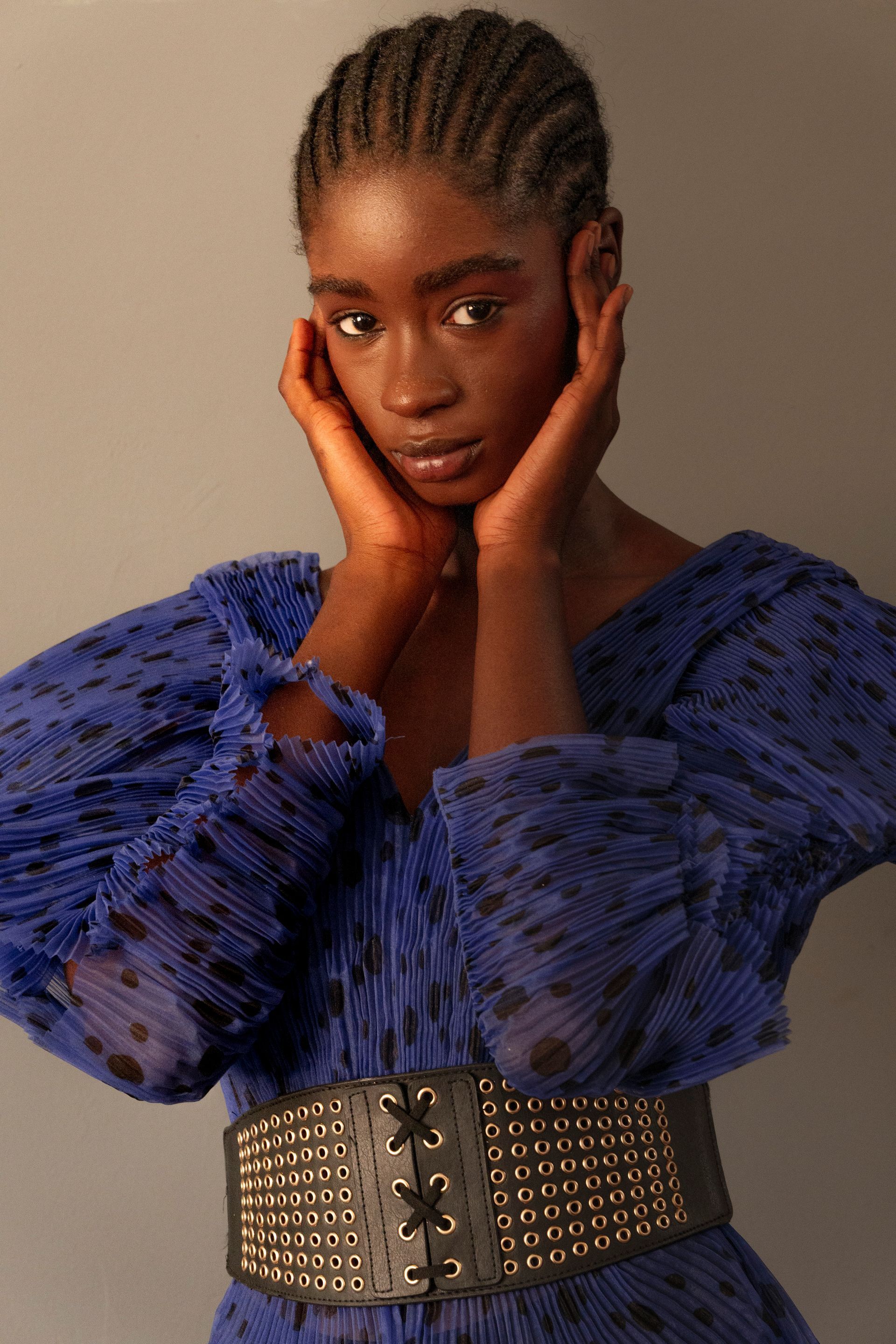 Donna dalla pelle scura che indossa un abito blu e una cintura nera e si tiene il viso tra le mani.