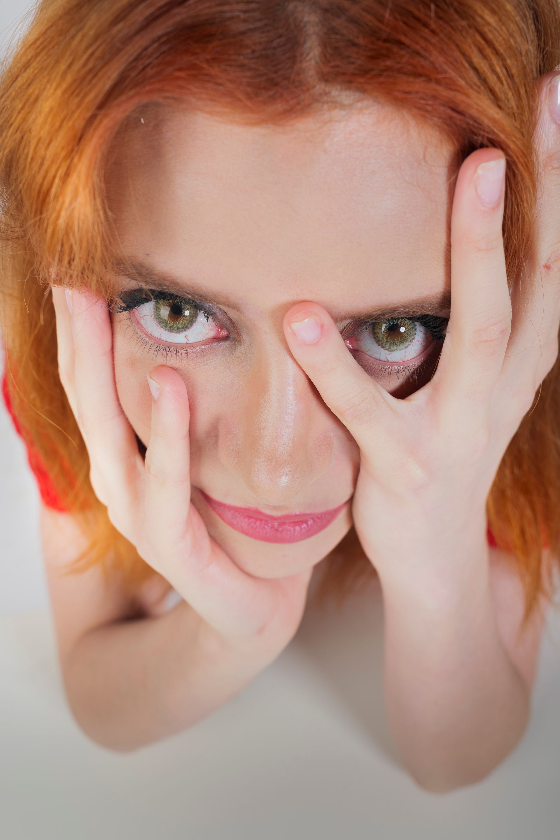 Donna con i capelli rossi e gli occhi verdi, che scruta da dietro le mani.