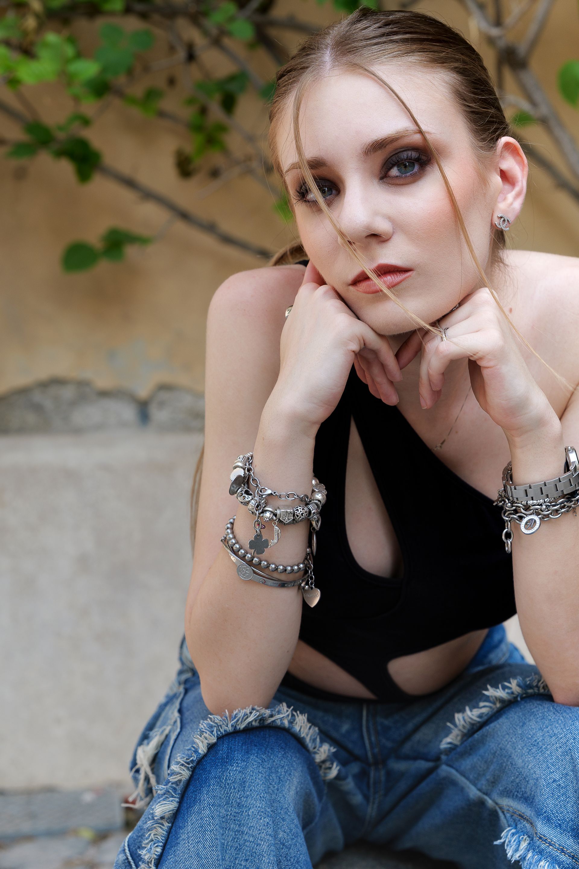 Donna con top nero e jeans strappati, mani sotto il mento, seduta all'aperto.