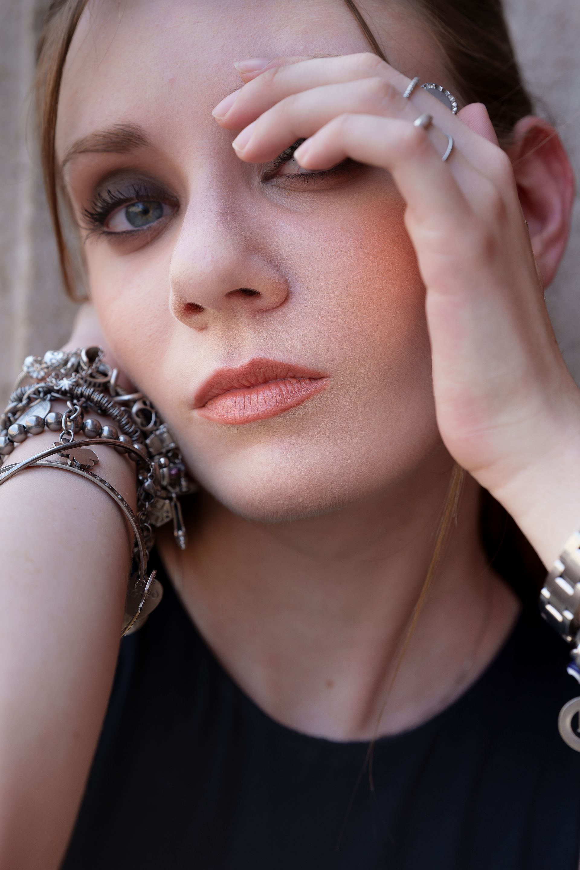 Donna con trucco scuro sugli occhi, molti braccialetti e anelli d'argento, viso toccante, espressione seria.