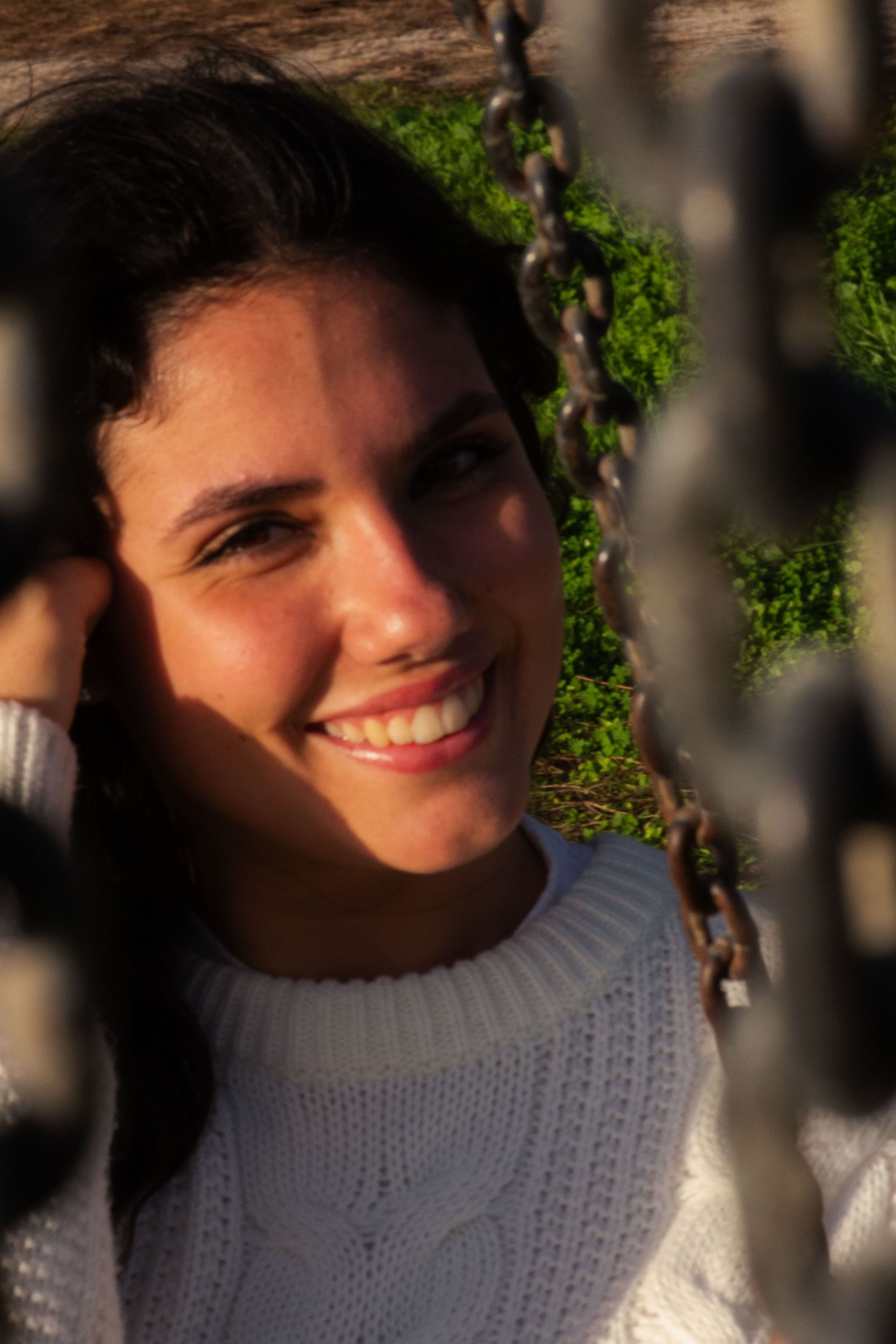 Giovane donna sorridente incorniciata da catene. Indossa un maglione bianco, all'aperto.