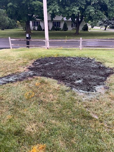 A large pile of dirt is sitting in the grass in front of a house.