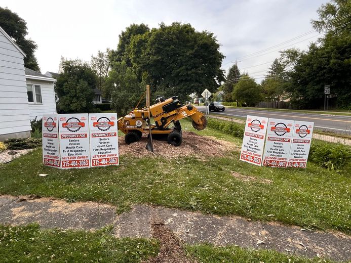 A stump grinder is being used to remove a tree stump in front of a house.