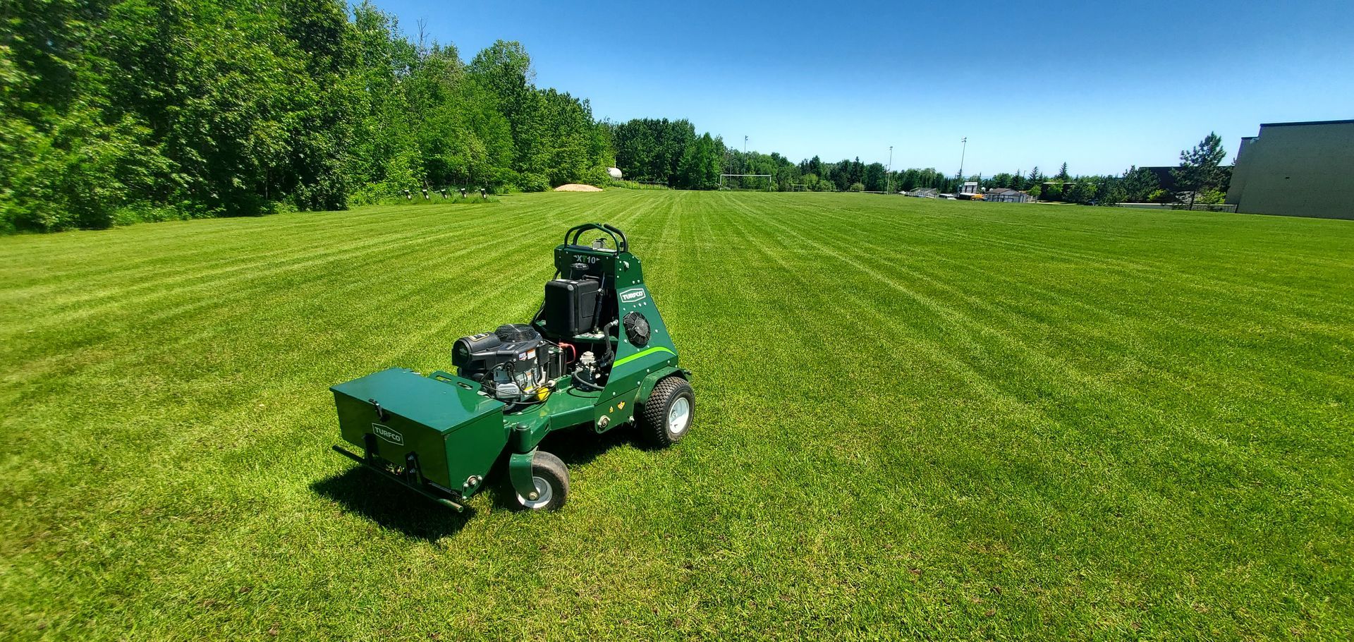 A green wheelbarrow filled with grass and leaves is sitting on top of a lush green lawn.