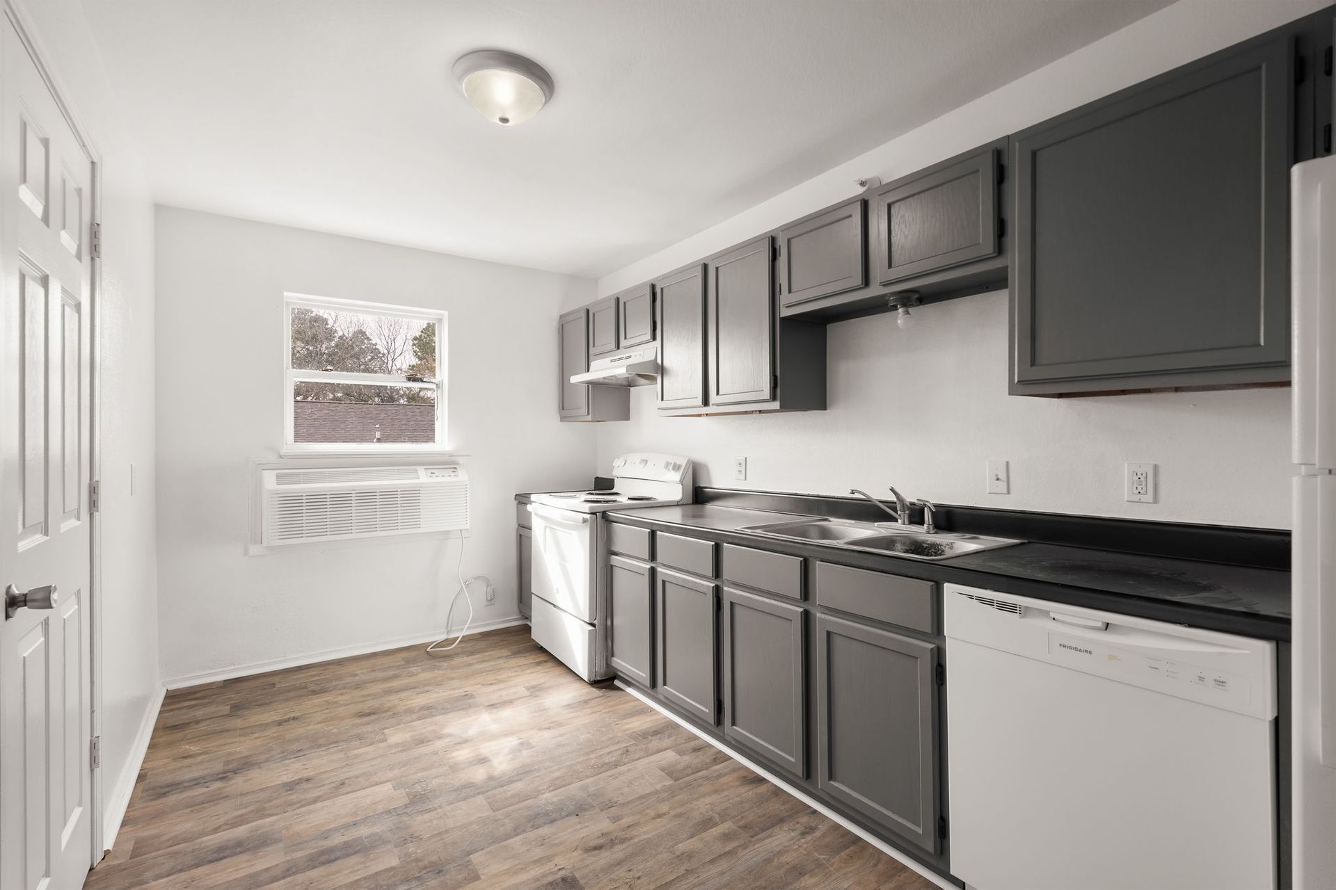 A kitchen with gray cabinets , white appliances , and a window.