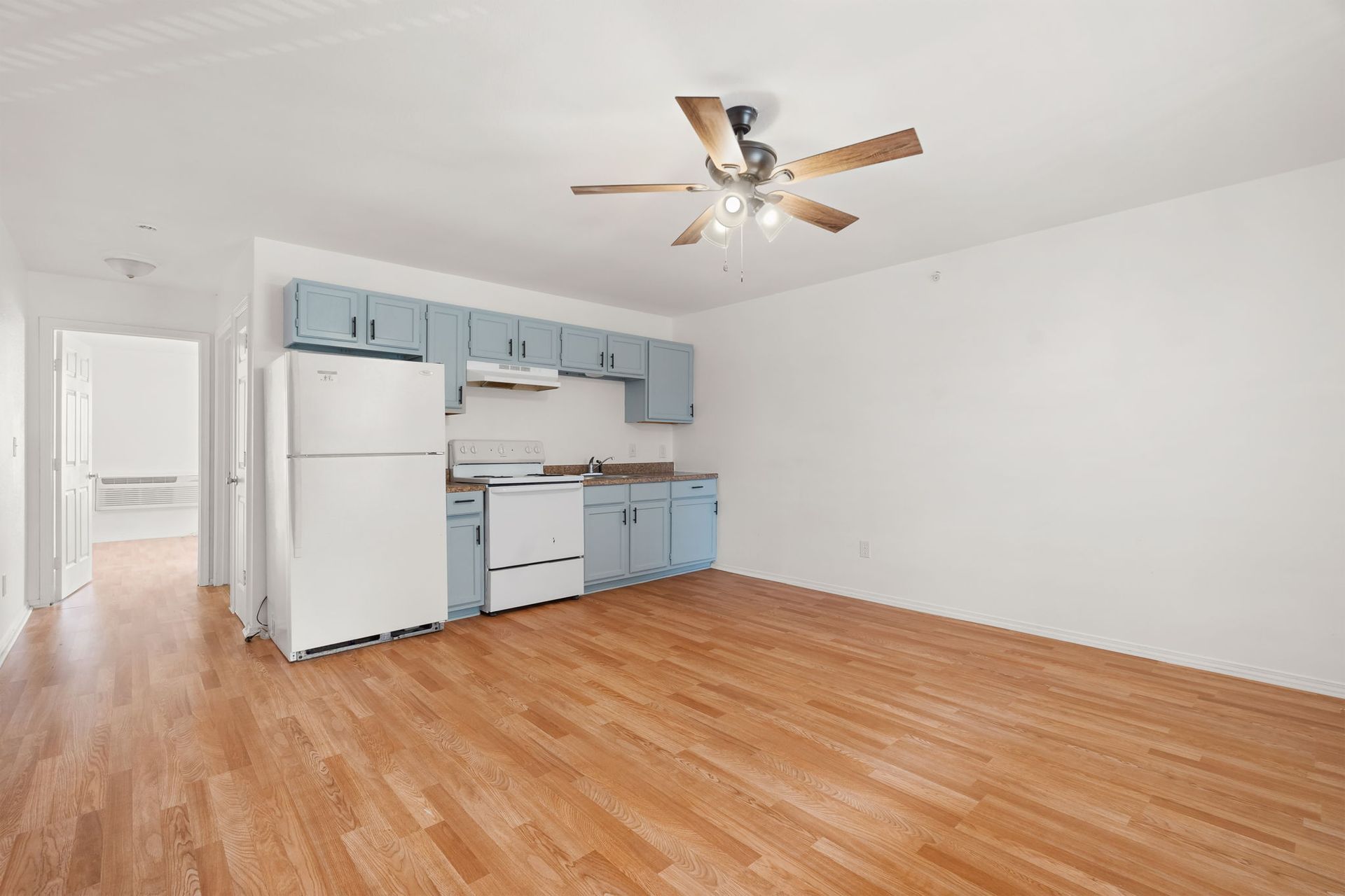 An empty kitchen with a refrigerator , stove , and ceiling fan.