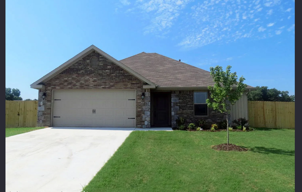 Tan brick home with attached garage, driveway, and green lawn under a blue sky.
