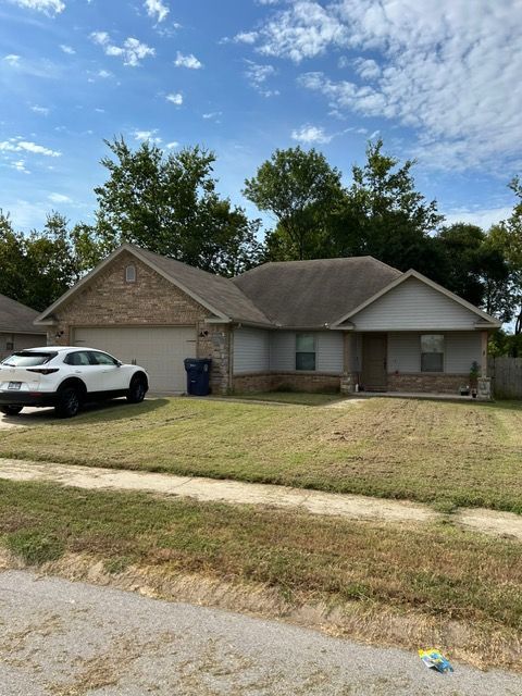 House with beige brick facade, garage, and parked white SUV. Green lawn, blue sky with some clouds.