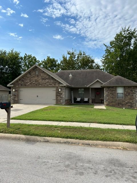 A one-story brick house with a green lawn and blue sky.