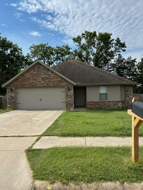 Tan one-story house with brick accents, two-car garage, and green lawn under a partly cloudy sky.