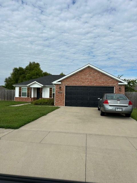 Brick house with black garage door; car parked in driveway, cloudy sky.
