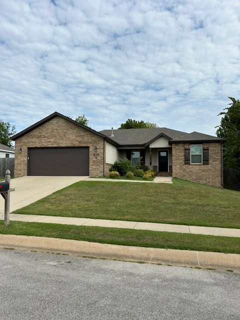 Brick house with brown garage door and shutters on a well-manicured lawn under a cloudy sky.