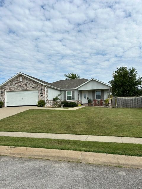 Residential house with brick and white exterior, green lawn, cloudy sky.