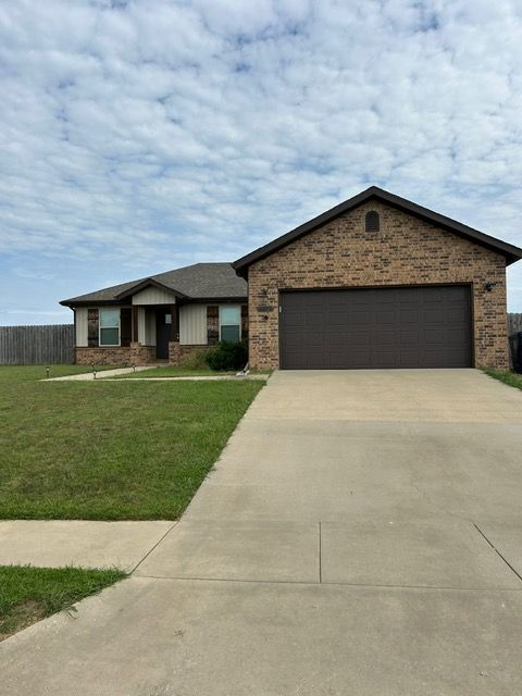 Tan brick house with a brown garage door and a long concrete driveway, cloudy sky.