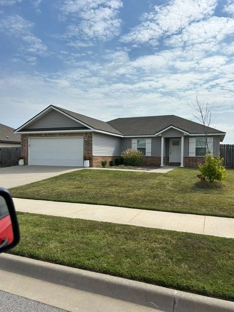 Gray and brick ranch-style house with a two-car garage, neat lawn, and blue sky.