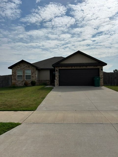 Single-story brick house with a dark garage door and driveway, under a cloudy sky.