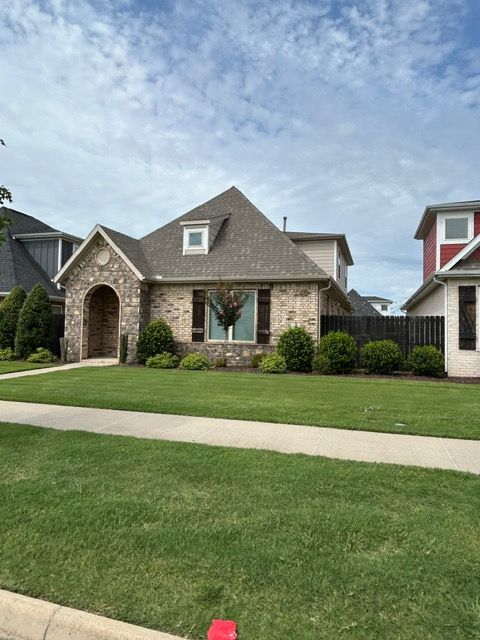 Brick house with green lawn, blue sky, and brown roof.