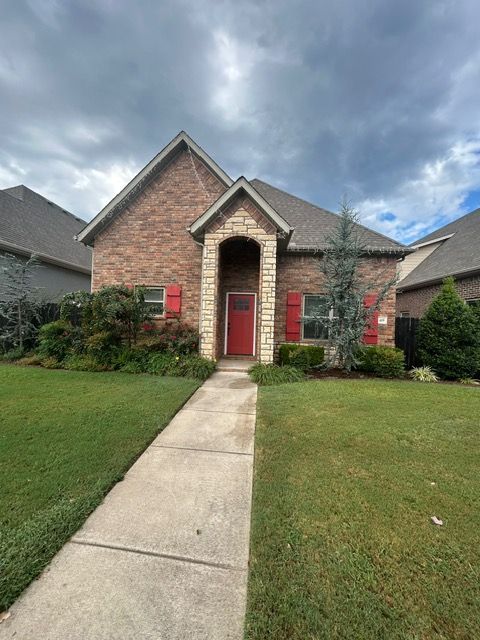 Brick house with red door and shutters, walkway through a green lawn. Cloudy sky.