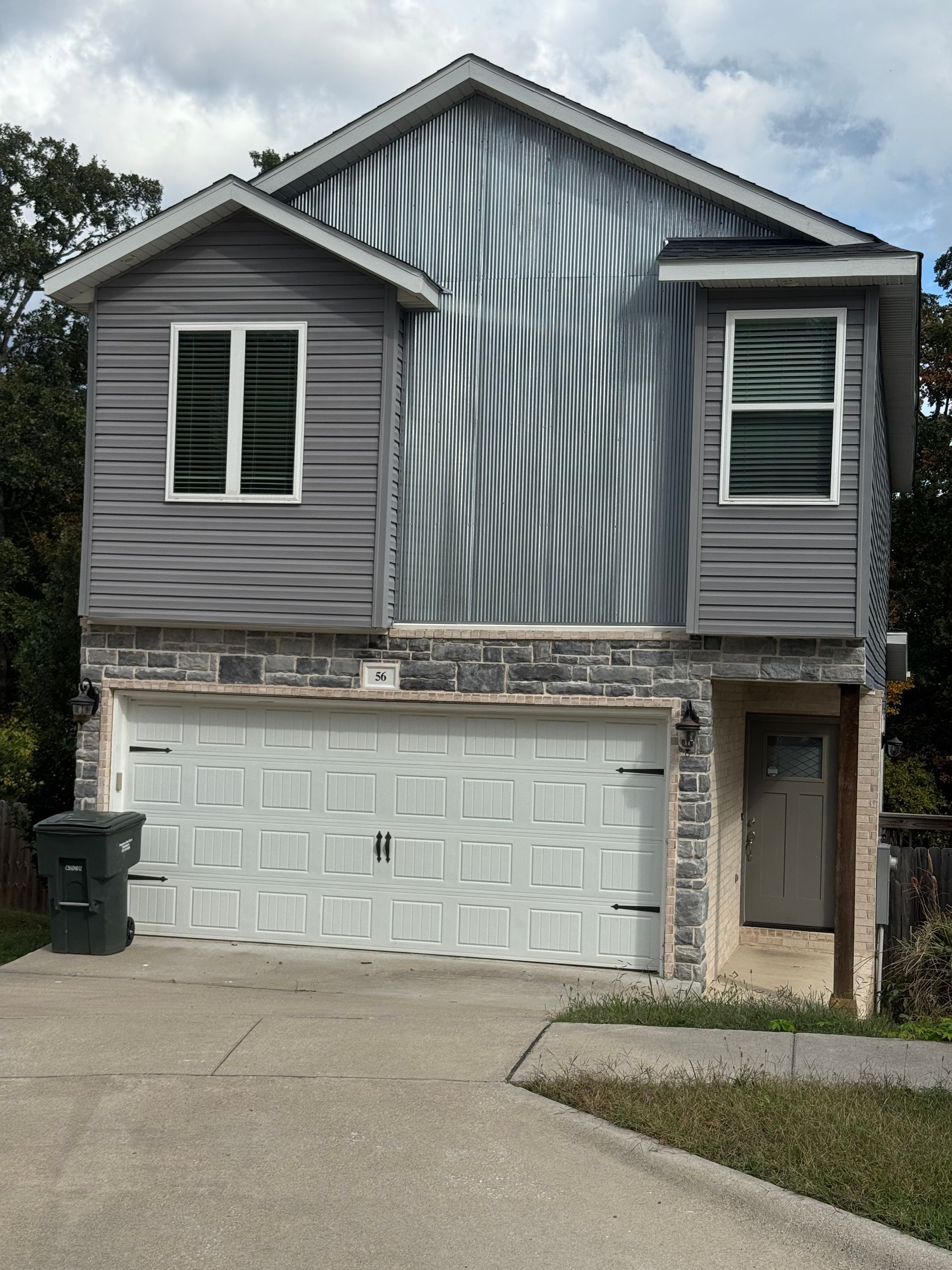 Gray two-story house with a garage and two upper windows. The house has textured siding and a driveway.
