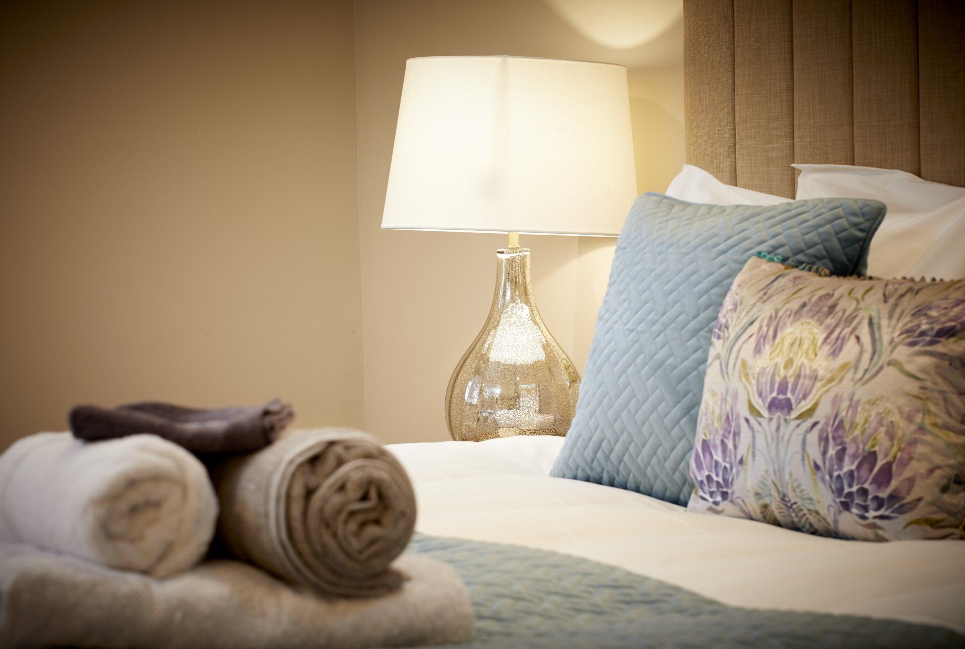 A bed with a lamp , pillows , blankets and towels on it.